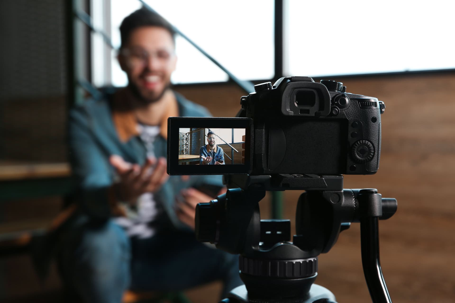 Man recording a testimonial-style video, sitting indoors and speaking in front of a camera on a tripod.